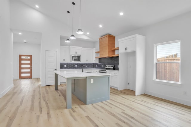 kitchen featuring decorative light fixtures, stainless steel appliances, a center island with sink, and white cabinetry