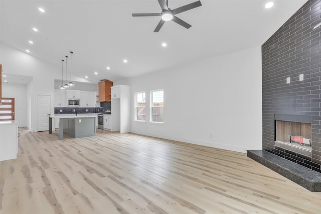 unfurnished living room with ceiling fan, light hardwood / wood-style flooring, high vaulted ceiling, and a fireplace