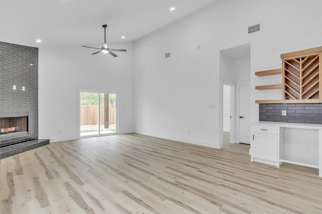 unfurnished living room featuring a towering ceiling, a brick fireplace, ceiling fan, and light hardwood / wood-style floors