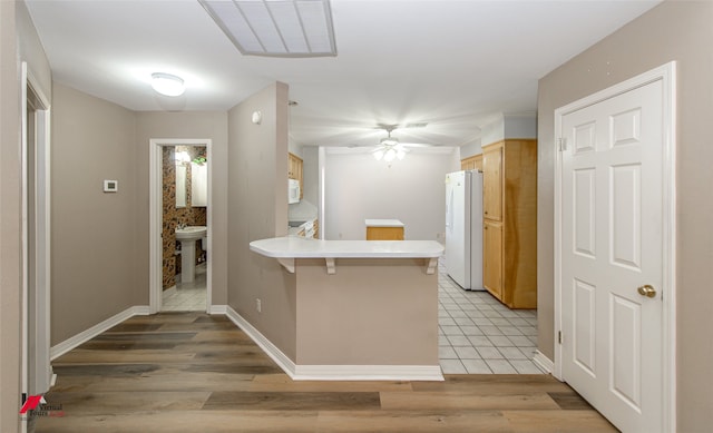 kitchen with light wood-type flooring, a kitchen breakfast bar, white appliances, and kitchen peninsula