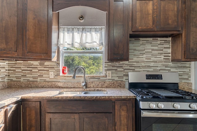 kitchen featuring stainless steel gas range oven, light stone countertops, sink, and decorative backsplash