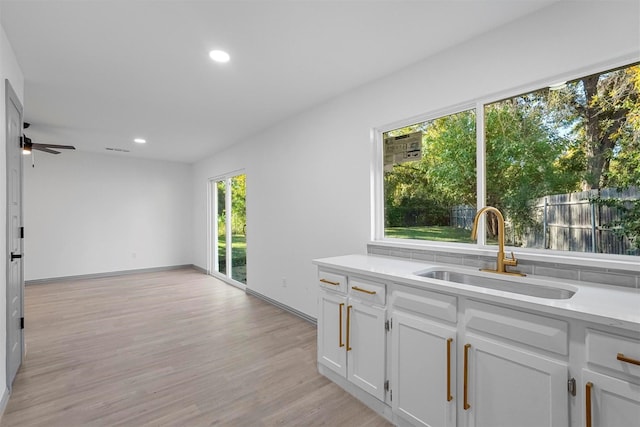 interior space featuring ceiling fan, sink, white cabinetry, and light wood-type flooring