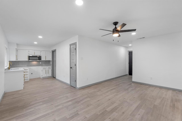 unfurnished living room featuring sink, light wood-type flooring, and ceiling fan