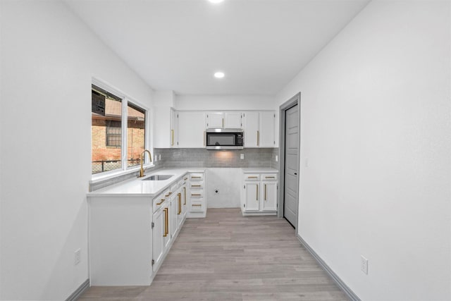 kitchen featuring sink, backsplash, white cabinets, and light wood-type flooring