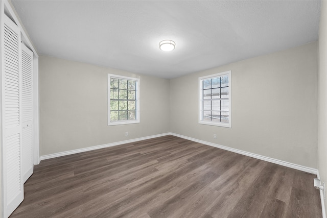 unfurnished bedroom with multiple windows, a closet, and dark hardwood / wood-style flooring