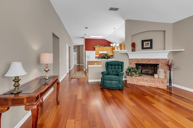 living area featuring a fireplace, wood-type flooring, vaulted ceiling, and a notable chandelier