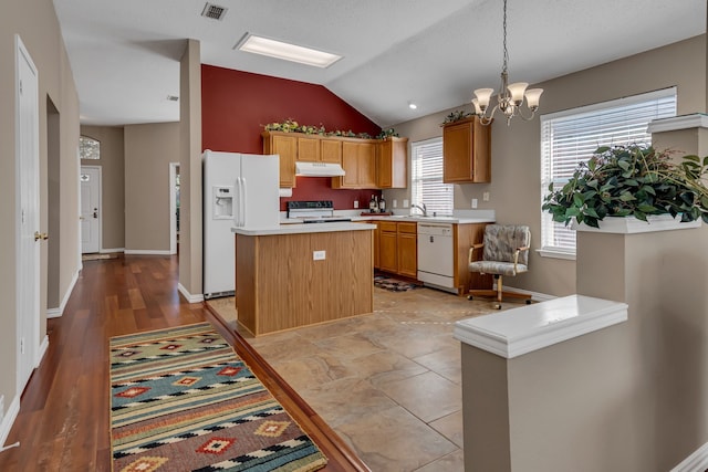 kitchen with white appliances, vaulted ceiling, an inviting chandelier, a kitchen island, and hanging light fixtures