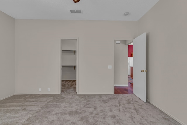 unfurnished bedroom featuring light carpet, a walk in closet, and a closet