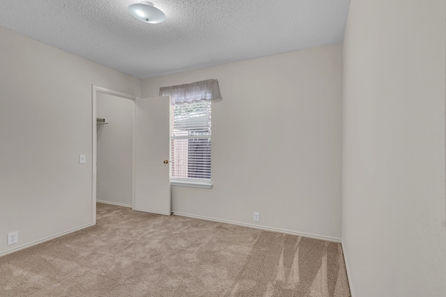 spare room featuring light colored carpet and a textured ceiling