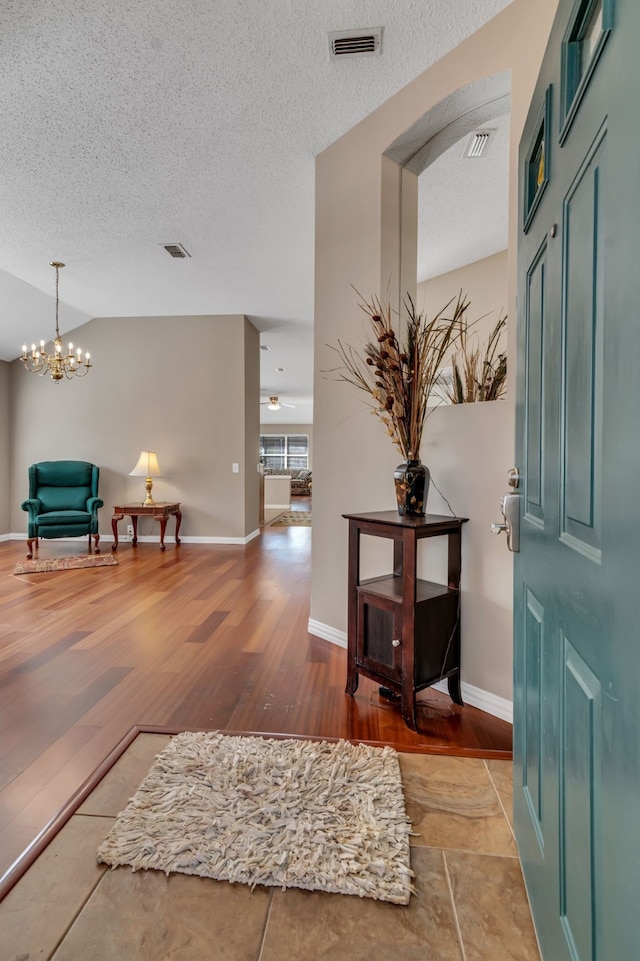 foyer with a notable chandelier, light hardwood / wood-style floors, a textured ceiling, and vaulted ceiling