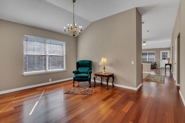 sitting room with plenty of natural light, ceiling fan with notable chandelier, wood-type flooring, and vaulted ceiling