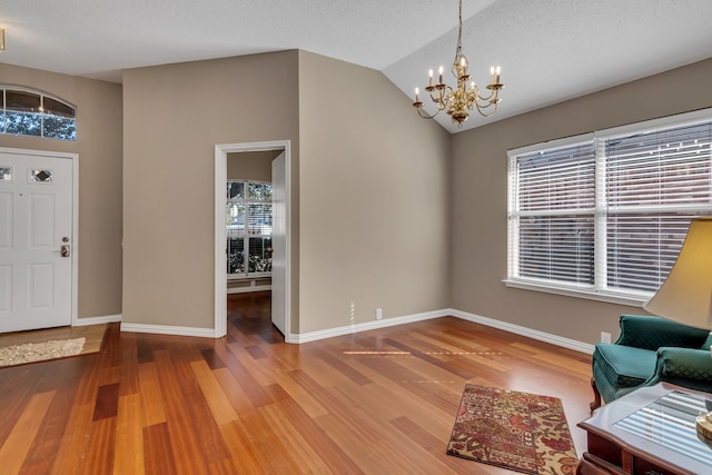 entryway featuring an inviting chandelier, wood-type flooring, a textured ceiling, and vaulted ceiling