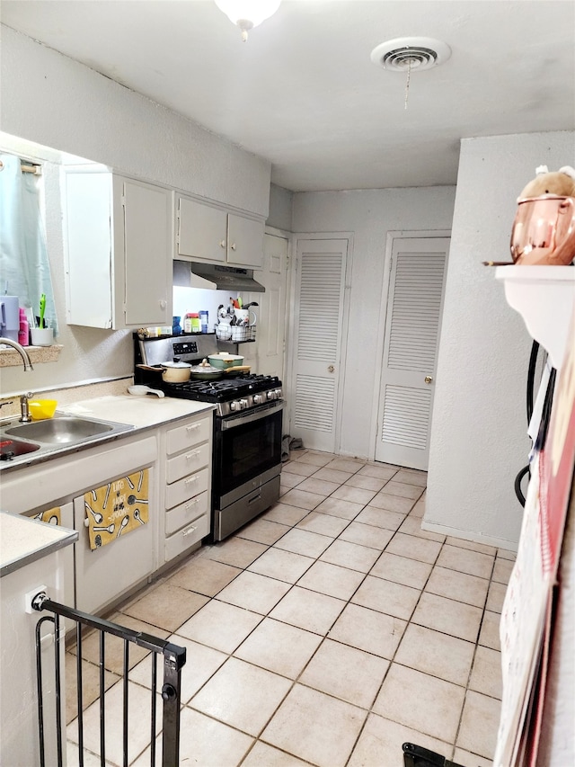 kitchen with white cabinets, light tile patterned floors, stainless steel gas range oven, and sink