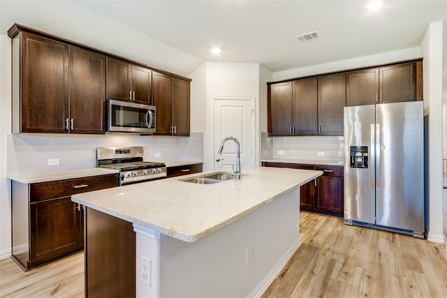 kitchen with light stone countertops, sink, stainless steel appliances, light hardwood / wood-style flooring, and a kitchen island with sink