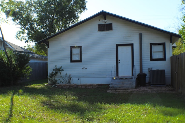 rear view of house featuring central AC unit and a lawn