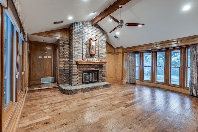 unfurnished living room with wood walls, lofted ceiling with beams, a brick fireplace, light hardwood / wood-style flooring, and ceiling fan