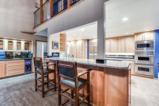 kitchen with stone counters, a kitchen breakfast bar, wine cooler, light brown cabinetry, and stainless steel appliances