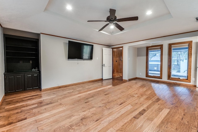 unfurnished living room with a raised ceiling, built in shelves, ceiling fan, and light wood-type flooring