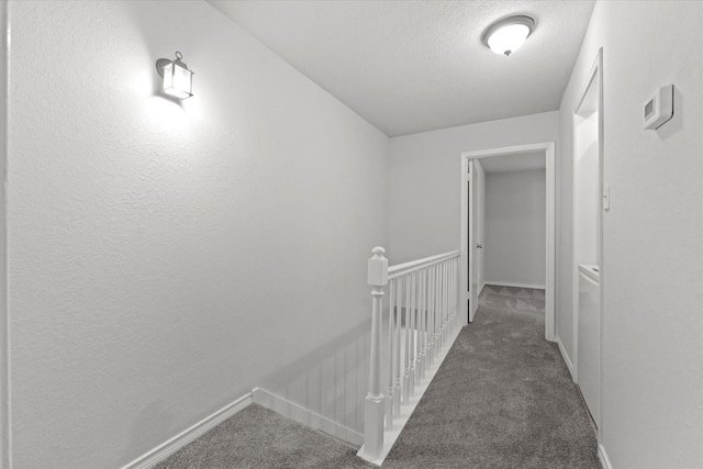 hallway with dark carpet and a textured ceiling