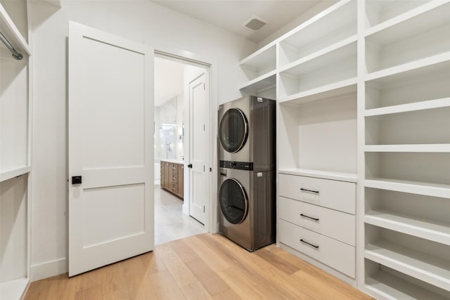 clothes washing area with stacked washer and dryer and light wood-type flooring