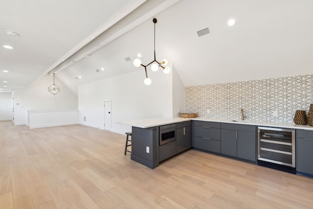 kitchen featuring vaulted ceiling with beams, decorative light fixtures, stainless steel microwave, kitchen peninsula, and beverage cooler