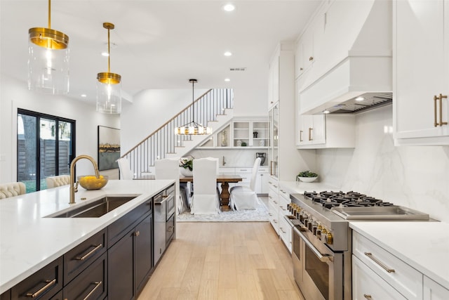 kitchen featuring sink, custom exhaust hood, white cabinetry, hanging light fixtures, and stainless steel appliances