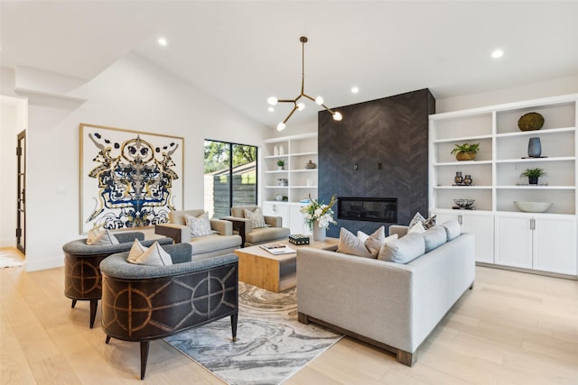 living room with a notable chandelier, a high end fireplace, light hardwood / wood-style flooring, and high vaulted ceiling