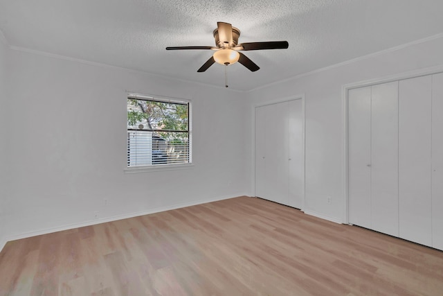 unfurnished bedroom with two closets, crown molding, ceiling fan, light wood-type flooring, and a textured ceiling