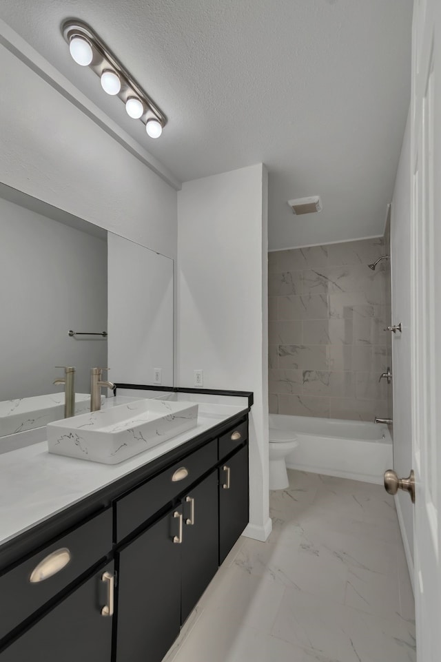 full bathroom with a textured ceiling, vanity, tiled shower / bath combo, and toilet