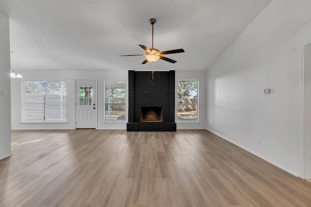 unfurnished living room featuring ceiling fan, a brick fireplace, hardwood / wood-style floors, a textured ceiling, and vaulted ceiling