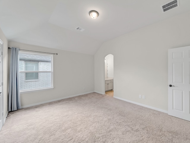 unfurnished bedroom featuring connected bathroom, light carpet, and vaulted ceiling