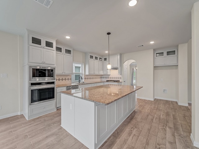 kitchen featuring a center island, light stone counters, white cabinetry, and light hardwood / wood-style flooring