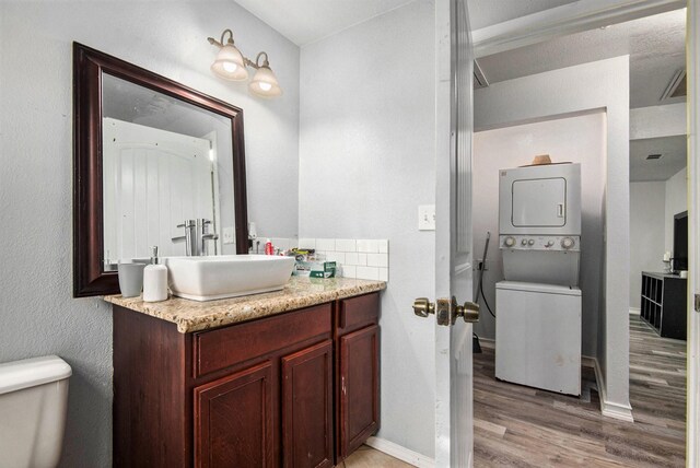 bathroom featuring hardwood / wood-style flooring, stacked washer and dryer, vanity, and toilet