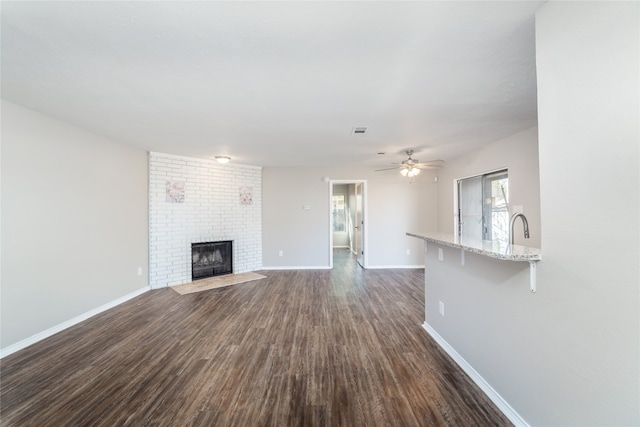 unfurnished living room featuring a fireplace, ceiling fan, and dark hardwood / wood-style flooring