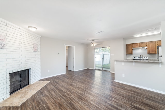 unfurnished living room with a fireplace, dark hardwood / wood-style flooring, ceiling fan, and sink