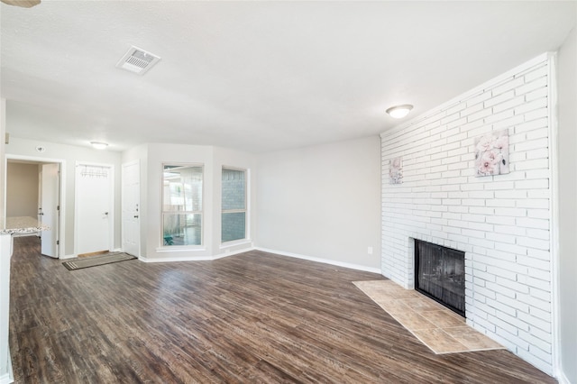 unfurnished living room featuring a brick fireplace and dark wood-type flooring