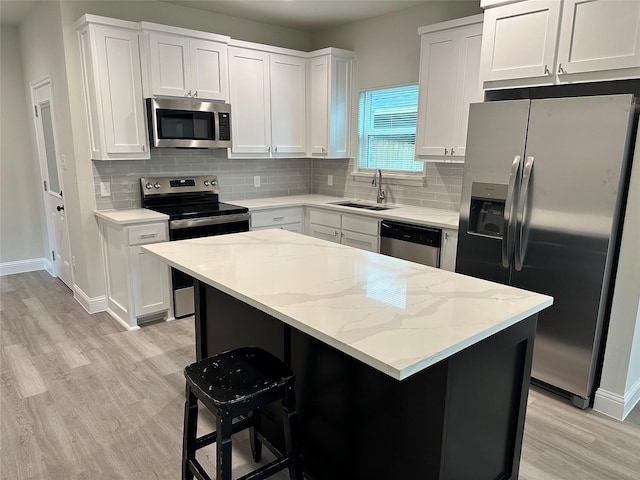 kitchen with white cabinets, a sink, stainless steel appliances, light wood-type flooring, and backsplash