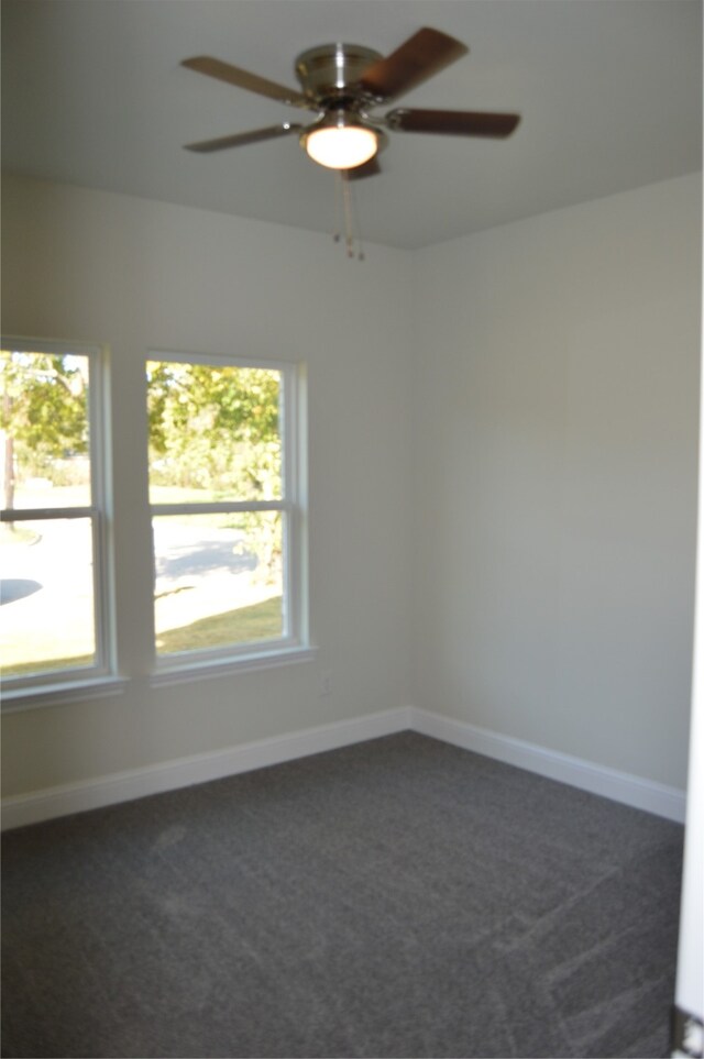 spare room featuring ceiling fan, dark carpet, and a wealth of natural light