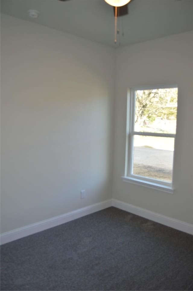empty room with dark colored carpet, a ceiling fan, and baseboards