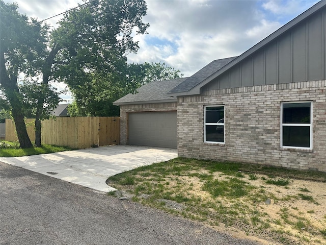 view of property exterior with fence, brick siding, board and batten siding, concrete driveway, and an attached garage