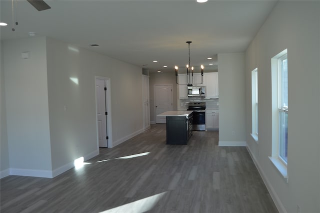 kitchen featuring white cabinetry, dark wood-type flooring, decorative light fixtures, a kitchen island, and appliances with stainless steel finishes