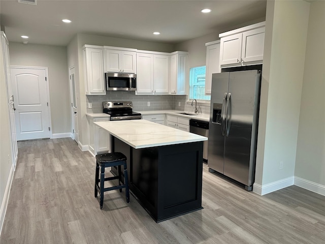 kitchen featuring white cabinets, light wood-style floors, a center island, stainless steel appliances, and decorative backsplash