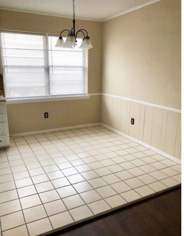 empty room featuring crown molding, light tile patterned floors, and a chandelier