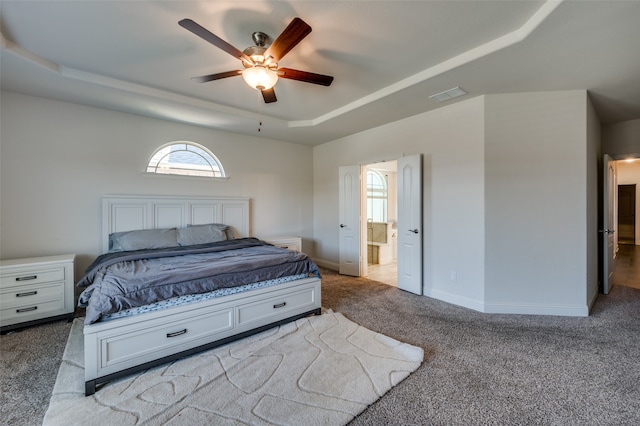 carpeted bedroom with ceiling fan, a raised ceiling, and ensuite bath