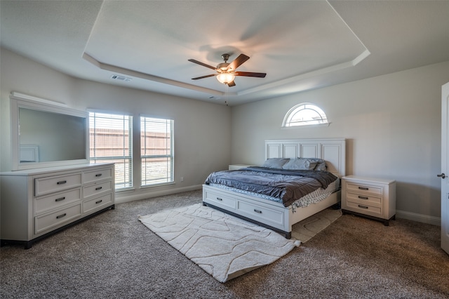 carpeted bedroom featuring a raised ceiling, multiple windows, and ceiling fan