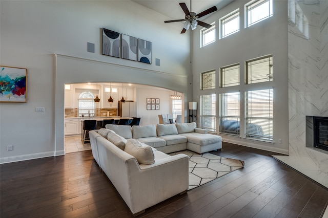 living room featuring dark hardwood / wood-style flooring, a towering ceiling, ceiling fan, sink, and a premium fireplace