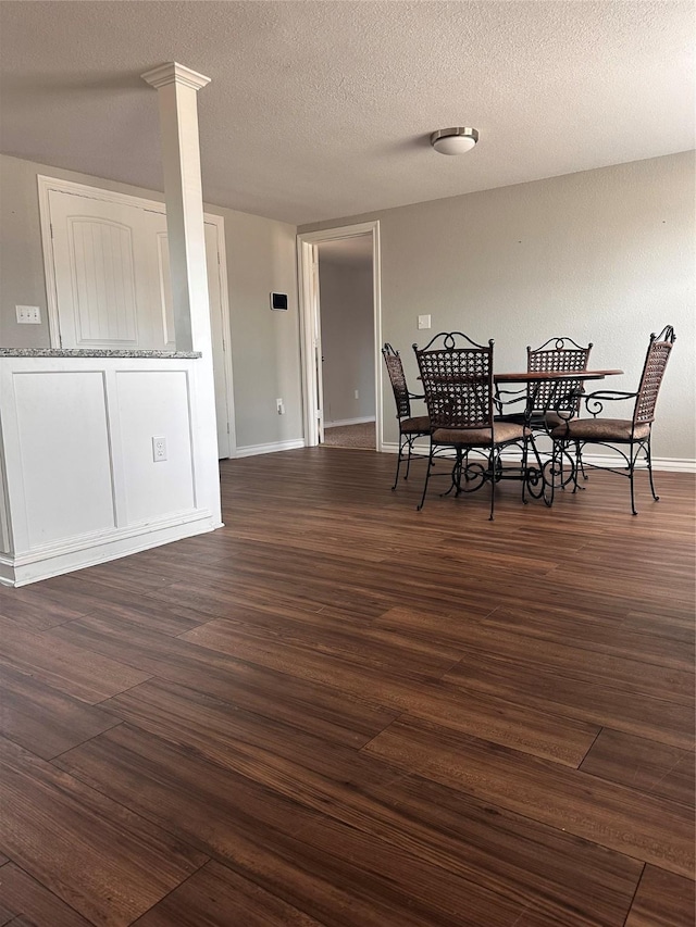 dining space with decorative columns, dark hardwood / wood-style flooring, and a textured ceiling