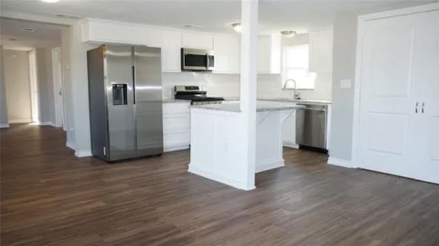 kitchen with appliances with stainless steel finishes, dark hardwood / wood-style flooring, sink, white cabinets, and a kitchen island