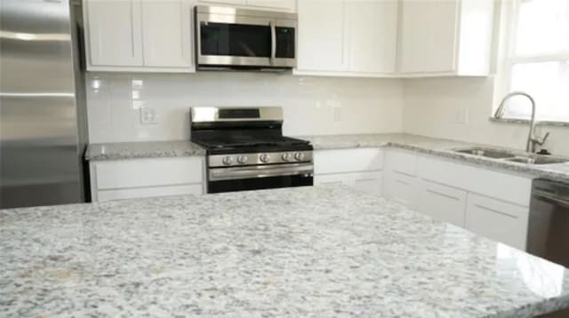 kitchen featuring white cabinetry, sink, light stone countertops, and appliances with stainless steel finishes