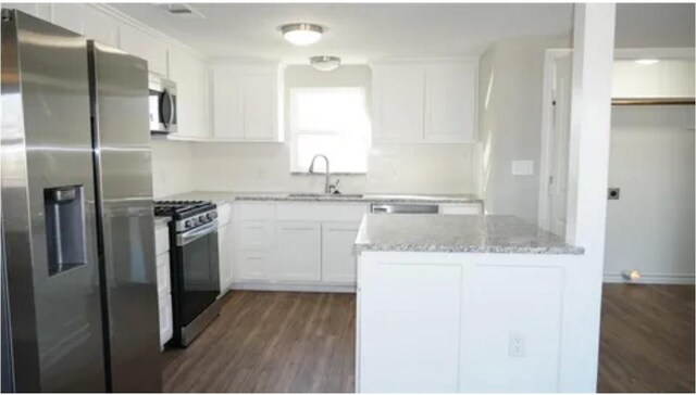 kitchen with appliances with stainless steel finishes, light stone counters, dark wood-type flooring, sink, and white cabinets